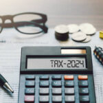 Word Tax 2024 on the calculator. Business and tax concept.Calculator, coins, book, tax form, and pen on table.Tax deduction planning.Financial research, government taxes, and calculation tax return